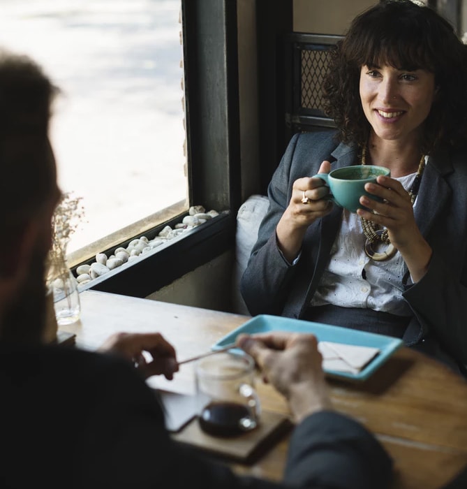 Mulher e homem sentados um de frente para o outro. Mulher feliz tomando café.